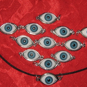 Könnte beinhalten: Eine Halskette mit mehreren silbernen Augenanhängern mit blauen Iris. Die Anhänger sind in einem Kreis auf einem roten Hintergrund angeordnet.