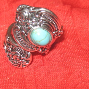 May include: A silver ring with an ornate design and a turquoise stone in the center.