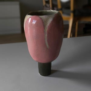 Puede incluir: Un jarrón de cerámica rosa y blanco con forma de tulipán y base negra.