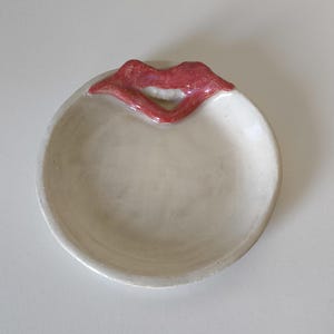 Puede incluir: Un plato de cerámica blanco con un diseño de labios esculpidos en rojo brillante.