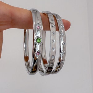 May include: Three silver bangle bracelets with decorative star and gem accents. The bracelets are stacked on top of each other.