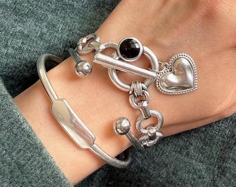 May include: A silver bracelet set with a heart charm, a black stone, and a toggle clasp.