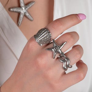 May include: A silver necklace with a starfish pendant and a set of three silver rings featuring a seashell, a starfish, and a wavy design.