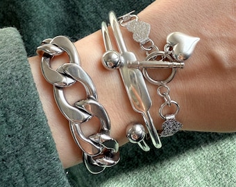May include: A set of four silver bracelets, one with a large chunky chain link design, one with a heart charm, and two with a simple bangle design.