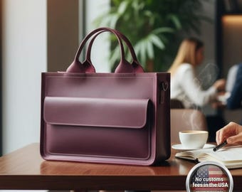 May include: A burgundy leather tote bag with a front flap pocket and two top handles. The bag is sitting on a wooden table in a cafe setting. The bag has a shoulder strap attachment.
