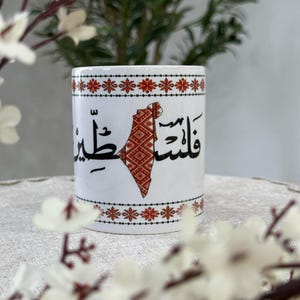 Palestinian map from traditional tatreez , and the word Palestine in Arabic . Ceramic coffee cup.