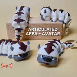 May include: Articulated Appa Avatar figures in white, gray, and maroon. The figures are on a light yellow surface, with one attached to a keychain. The figures are segmented, allowing for movement. The text "ARTICULATED APPA - AVATAR" is visible.