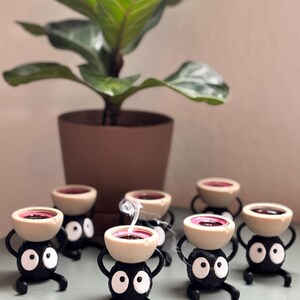 Adorable 3D-printed Soot Sprite tealight holder inspired by Studio Ghibli. This black and white candle holder features a cute soot spirit figure holding a small tealight, creating a cozy, magical ambiance. Perfect for anime fans, home decor lovers, and unique gift ideas. Add a touch of whimsy to your space with this handcrafted, geeky candle holder. Great for desks, shelves, or nightstands!
