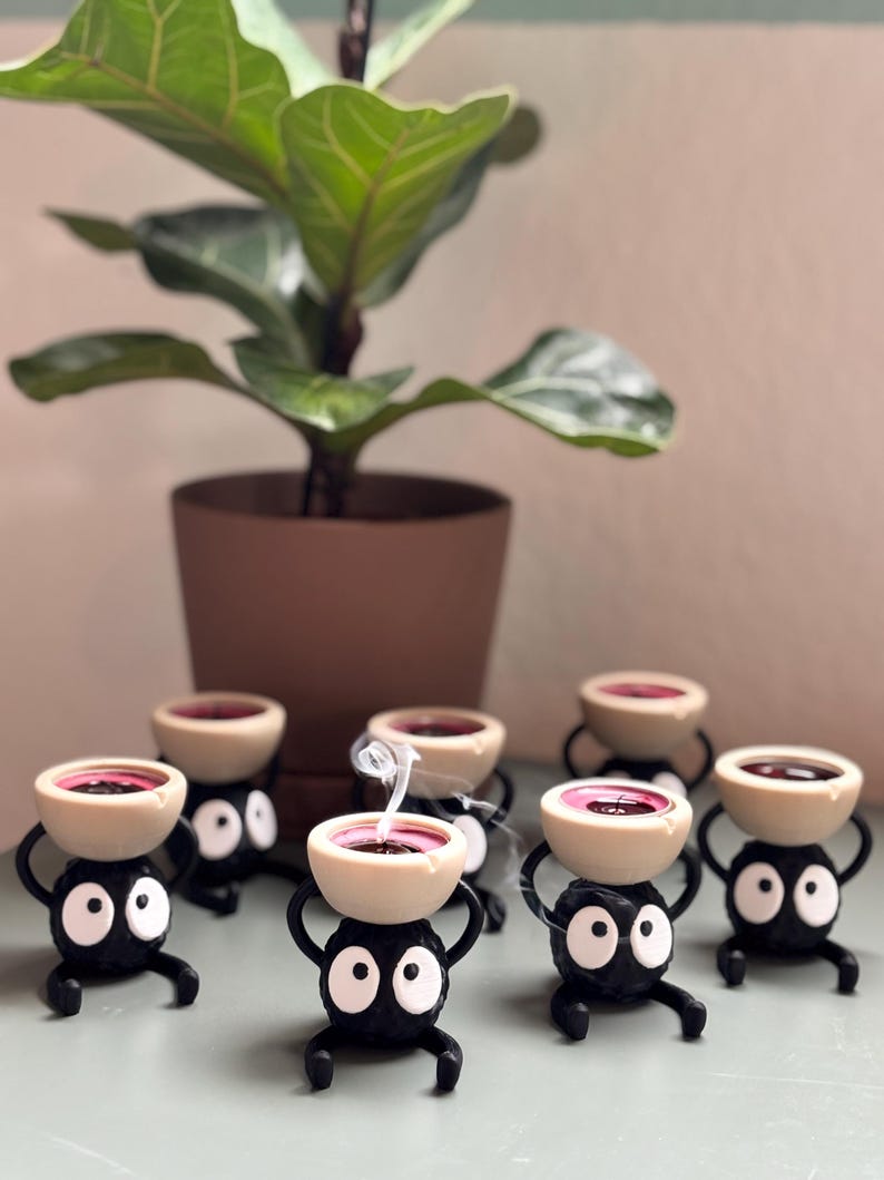 Adorable 3D-printed Soot Sprite tealight holder inspired by Studio Ghibli. This black and white candle holder features a cute soot spirit figure holding a small tealight, creating a cozy, magical ambiance. Perfect for anime fans, home decor lovers, and unique gift ideas. Add a touch of whimsy to your space with this handcrafted, geeky candle holder. Great for desks, shelves, or nightstands!