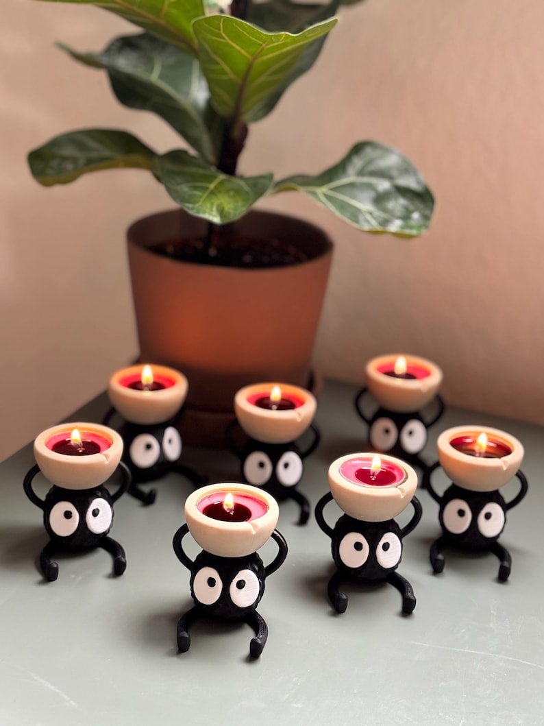 Adorable 3D-printed Soot Sprite tealight holder inspired by Studio Ghibli. This black and white candle holder features a cute soot spirit figure holding a small tealight, creating a cozy, magical ambiance. Perfect for anime fans, home decor lovers, and unique gift ideas. Add a touch of whimsy to your space with this handcrafted, geeky candle holder. Great for desks, shelves, or nightstands!