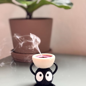 Adorable 3D-printed Soot Sprite tealight holder inspired by Studio Ghibli. This black and white candle holder features a cute soot spirit figure holding a small tealight, creating a cozy, magical ambiance. Perfect for anime fans, home decor lovers, and unique gift ideas. Add a touch of whimsy to your space with this handcrafted, geeky candle holder. Great for desks, shelves, or nightstands!