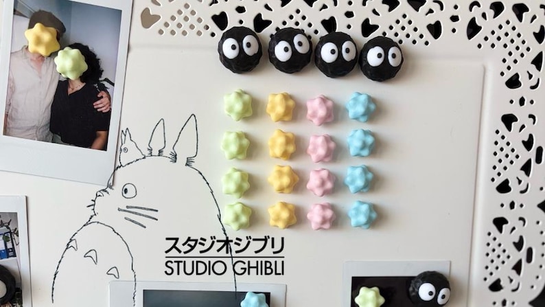 Könnte beinhalten: Eine weiße dekorative Tafel mit Studio Ghibli-Kunstwerken und Charaktermagneten. Die Magnete umfassen schwarze Rußgeister und farbenfrohe sternförmige Designs in Pastelltönen von Grün, Gelb, Rosa und Blau. Es gibt auch ein Foto.