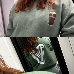 Puede incluir: Dos sudaderas verdes con dise&ntilde;os diferentes. Una sudadera tiene un logotipo de Guinness bordado en blanco en la parte delantera. La otra sudadera tiene un logotipo de arpa bordado en blanco en la parte posterior.