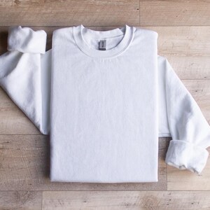 Puede incluir: Una camiseta blanca de manga larga doblada sobre una superficie de madera.