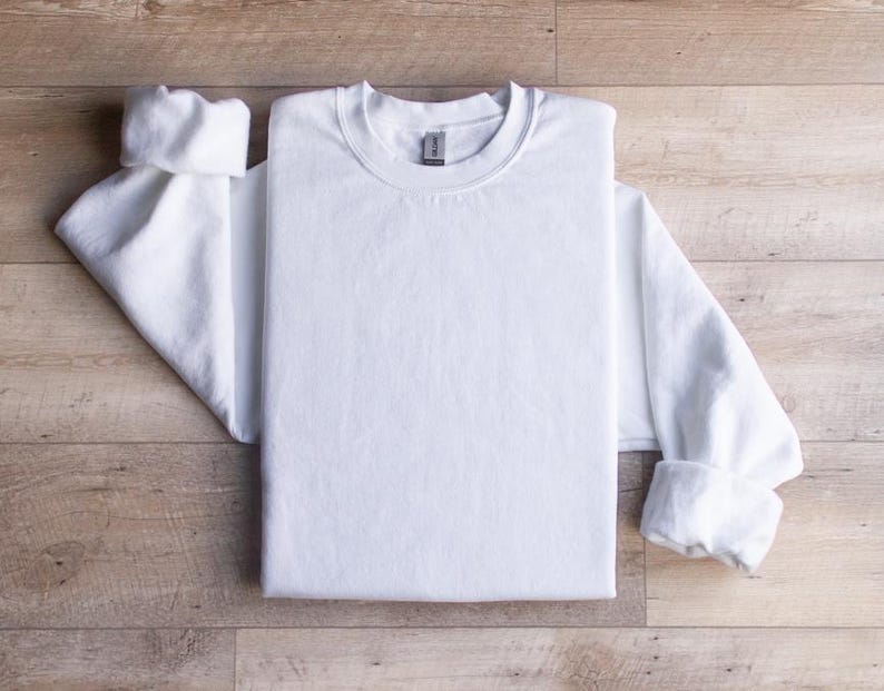 Puede incluir: Una camiseta blanca de manga larga doblada sobre una superficie de madera.