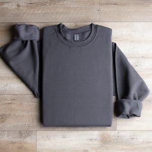 Puede incluir: Una sudadera gris antracita doblada sobre una superficie de madera.