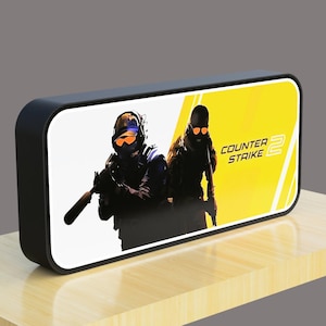 May include: Black and yellow rectangular speaker with a graphic of two people wearing tactical gear and the text "COUNTER STRIKE 2".