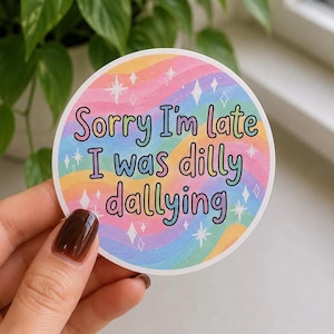 Könnte beinhalten: Ein runder Aufkleber mit pastellfarbenem Regenbogenhintergrund und dem Text "Sorry I'm late I was dilly dallying" in bunten Buchstaben. Der Aufkleber hat Stern- und Diamantakzente.