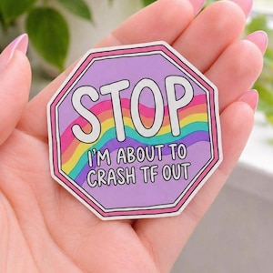 May include: A sticker with a purple octagon shape and a pink border. The word "STOP" is in white block letters at the top. Below, the text "I'M ABOUT TO CRASH TF OUT" is written over a rainbow design.