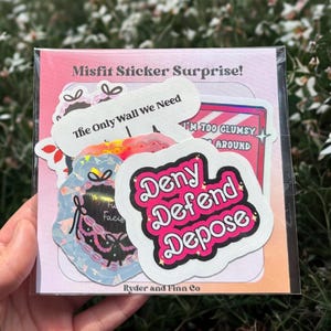 May include: A set of 7 colorful stickers with various designs and phrases, including "The Only Wall We Need", "I'm Too Clumsy Around", and "Deny Defend Depose". The stickers are packaged in a clear plastic bag with a pink and white background.