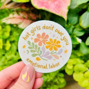 Hand holding a round retro floral vinyl sticker that reads, “Hot girls don’t owe you emotional labor.” Feminist empowerment sticker featuring pastel flowers, botanical accents, and soft vintage colors. Perfect for laptops, water bottles, Kindles, journals, planners, notebooks, and gifts for feminists, therapists, counselors, and women embracing healthy boundaries.