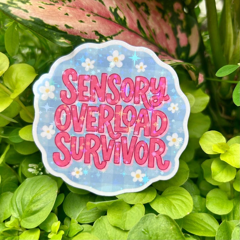 Glossy holographic vinyl sticker reading “Sensory Overload Survivor” displayed among vibrant green leaves in natural sunlight. Features bold pink retro typography, a pastel blue background, white daisies, and shimmering star accents, highlighting the sticker’s neurodiversity theme, sensory overload awareness, and premium holographic vinyl finish.