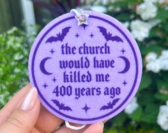 Pode incluir: Um ornamento circular de feltro lavanda com texto roxo escuro que diz: "the church would have killed me 400 years ago". O design inclui morcegos, luas crescentes e estrelas roxas, com uma pequena conta de estrela iridescente no topo.