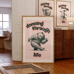 Puede incluir: Tres impresiones artísticas enmarcadas con un fondo rosa y las palabras "dancing through life". Una impresión presenta un oso bailando, otra un caimán bailando y la tercera un pingüino bailando. Las impresiones tienen un marco de madera.