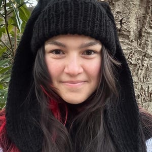 Puede incluir: Un gorro de punto negro con largas orejas de conejo. El gorro lo lleva una persona con el pelo largo y oscuro con reflejos rosas.