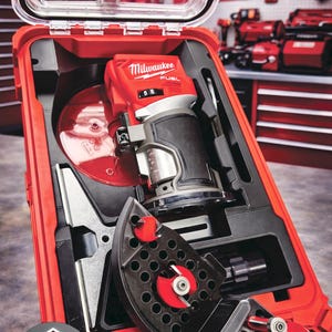 May include: A red Milwaukee FUEL router kit in a red case. The kit includes a router, various attachments, and accessories. The case is open, revealing the tools neatly organized within. The background shows a workshop setting with other tools.