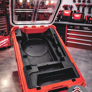 May include: Open red tool case with a clear lid, revealing a black interior with various compartments. The case is designed to hold tools and equipment. The Milwaukee logo is visible in the background.
