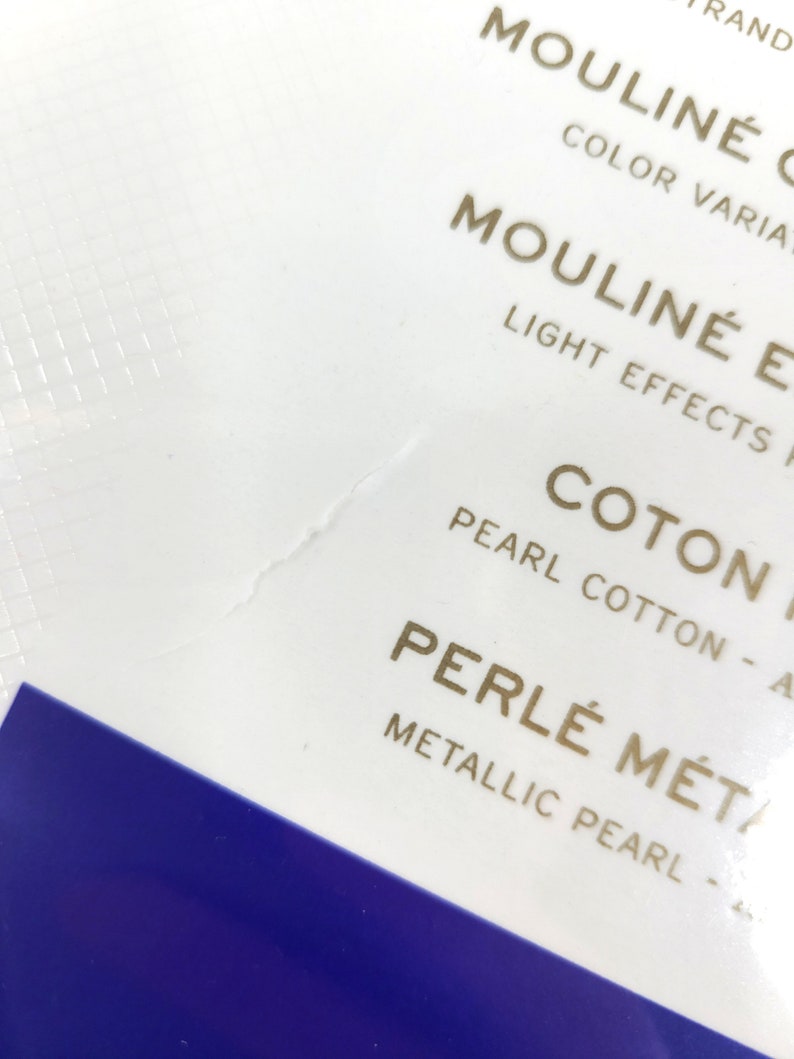 May include: Close-up of a white label with gold text that reads "Mouline'  Color Variations", "Mouline'  Light Effects", "Coton Pearl Cotton", and "Perle'  Metallic Pearl".