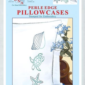 May include: White Perle Edge pillowcases stamped for embroidery with beach-themed designs. The pillowcases feature a seashell, a turtle, and a starfish. The package includes the text "PERLE EDGE PILLOWCASES" and "Stamped for Embroidery".