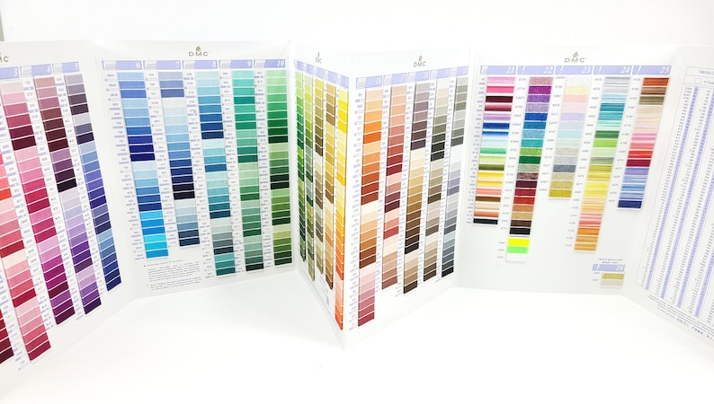 May include: A DMC color chart with a variety of thread colors organized by color family. The chart is folded in half and shows a wide range of colors, including red, blue, green, yellow, brown, and gray.