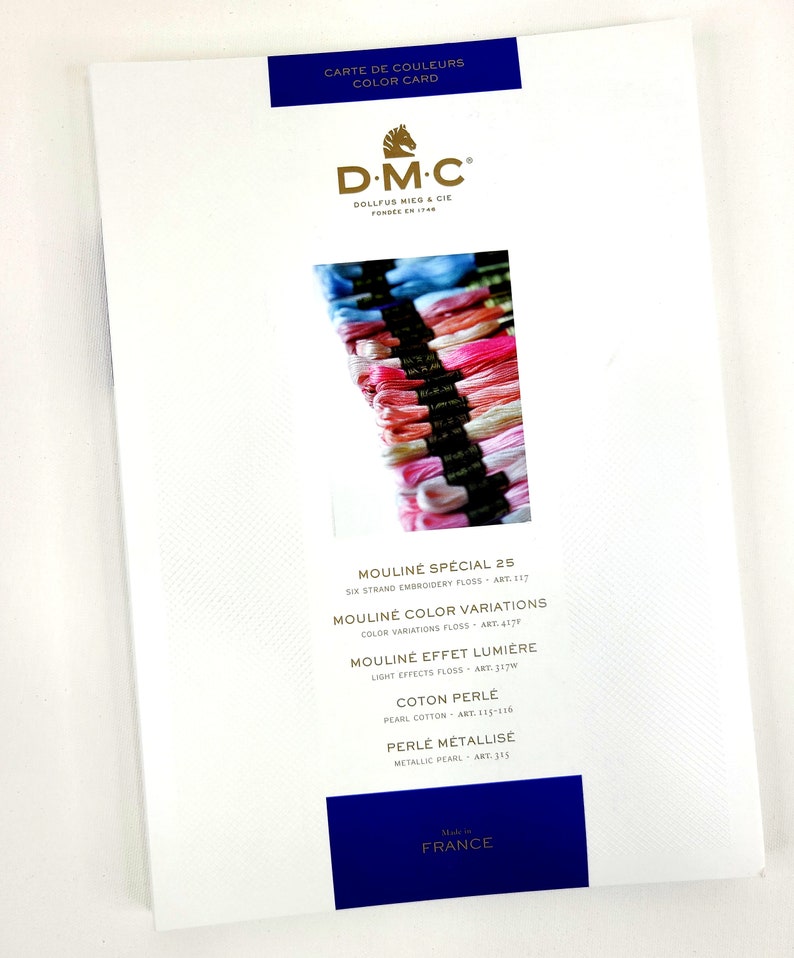 May include: DMC embroidery floss color card featuring a variety of colors, including pink, blue, and white. The card includes the brand name DMC, the company's founding date, and the names of different types of floss, including Moulin&eacute; Sp&eacute;cial 25, Moulin&eacute; Color Variations, Moulin&eacute; Effet Lumi&egrave;re, Coton Perle, and Perle M&eacute;tallis&eacute;.