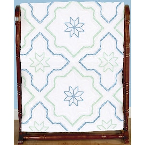 May include: A white quilt with a geometric pattern in blue and green, displayed on a wooden quilt rack. The quilt features star-like designs and a repeating pattern. The wooden rack is a dark brown color.