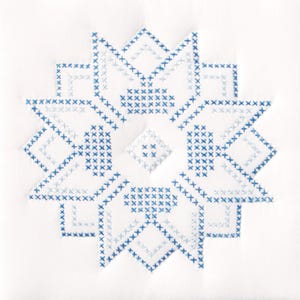 May include: A white textile featuring a large, symmetrical star design. The star is composed of blue cross-stitch embroidery, with varying shades of blue creating depth and detail. The design is centered on the fabric.