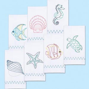 K&ouml;nnte beinhalten: Wei&szlig;e Handt&uuml;cher mit Stickereien von Meeresmotiven. Die Designs zeigen ein Seepferdchen, einen Fisch, eine Muschel, einen Seestern und eine Schildkr&ouml;te. Jedes Handtuch hat eine dekorative Bord&uuml;re. Die Stickerei verwendet blaue, gr&uuml;ne, gelbe und rote F&auml;den.