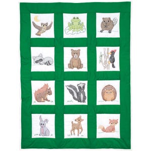 May include: A green and white patchwork quilt featuring embroidered woodland animals. The quilt showcases an owl, frog, beaver, raccoon, bear, woodpecker, squirrel, skunk, hedgehog, rabbit, deer, and fox. The quilt is a charming addition to a nursery.