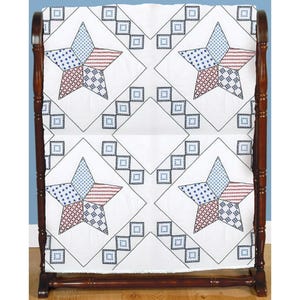 May include: A white quilt with a star pattern in red, white, and blue, displayed on a wooden quilt rack. The stars are composed of various geometric patterns. The quilt rack is made of dark wood.