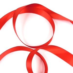 May include: A red satin ribbon is curled and twisted on a white background.