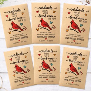 May include: Six rectangular kraft paper seed packets featuring a red cardinal illustration on a branch. Text reads: cardinals APPEAR WHEN loved ones ARE NEAR. Below: Wildflower seeds planted with love in memory of DAVID MICHAEL THOMPSON 03.22.1950 - 05.12.2026.
