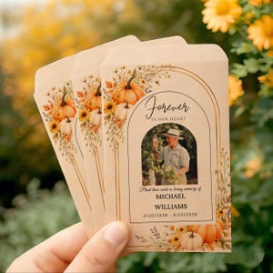 May include: Three light brown paper seed packets featuring an arched gold frame, watercolor pumpkins, and wildflowers. The text reads Forever in our heart, Plant these seeds in loving memory of MICHAEL WILLIAMS 2/10/1938 - 5/15/2026, with a photo.