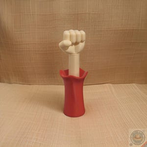 May include: A red plastic vase with a white fist coming out of the top.