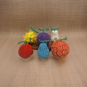 May include: Six different colored fruit-shaped figurines with green stems. The figurines are made of a smooth, textured material and are arranged in a semi-circle on a wooden surface.