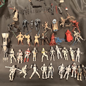K&ouml;nnte beinhalten: Eine Sammlung von Star Wars-Actionfiguren, darunter Sturmtruppen, Jedi und verschiedene andere Charaktere. Die Figuren sind in verschiedenen Posen und weisen detaillierte Designs auf. Die Farbpalette umfasst Wei&szlig;, Schwarz, Rot und Beige.