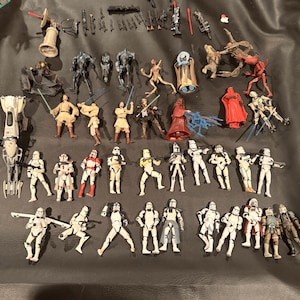 K&ouml;nnte beinhalten: Eine Sammlung von Star Wars-Actionfiguren und Zubeh&ouml;r, darunter verschiedene Charaktere und Waffen. Die Figuren sind in verschiedenen Posen und Farben, mit Fokus auf den ikonischen Charakteren der Franchise.