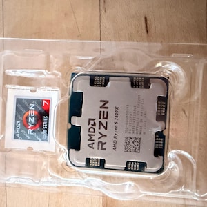 May include: A new AMD Ryzen 5 7600X processor and a Ryzen 7 7000 Series processor in a clear plastic package. The Ryzen 5 processor has the AMD Ryzen logo and model information printed on it. The Ryzen 7 processor has the Ryzen 7 logo.