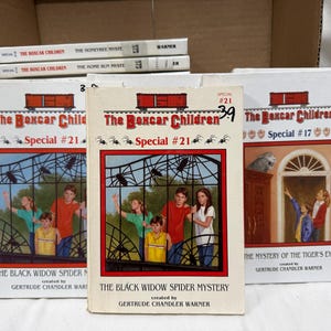 Puede incluir: Una colección de libros antiguos de "The Boxcar Children". Las portadas presentan ilustraciones de niños y los títulos "The Black Widow Spider Mystery" y "The Mystery of the Tiger's Eye". Los libros están en una caja de cartón.