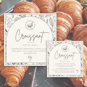 May include: Two white labels with black text and illustrations of leaves and a bowl with a spoon. The labels are for "Croissant Original" and list the ingredients, including wheat flour, butter, cream, salt, yeast, milk, sugar, and salt. The labels also state that the croissants contain wheat and milk. The labels are 80g each.